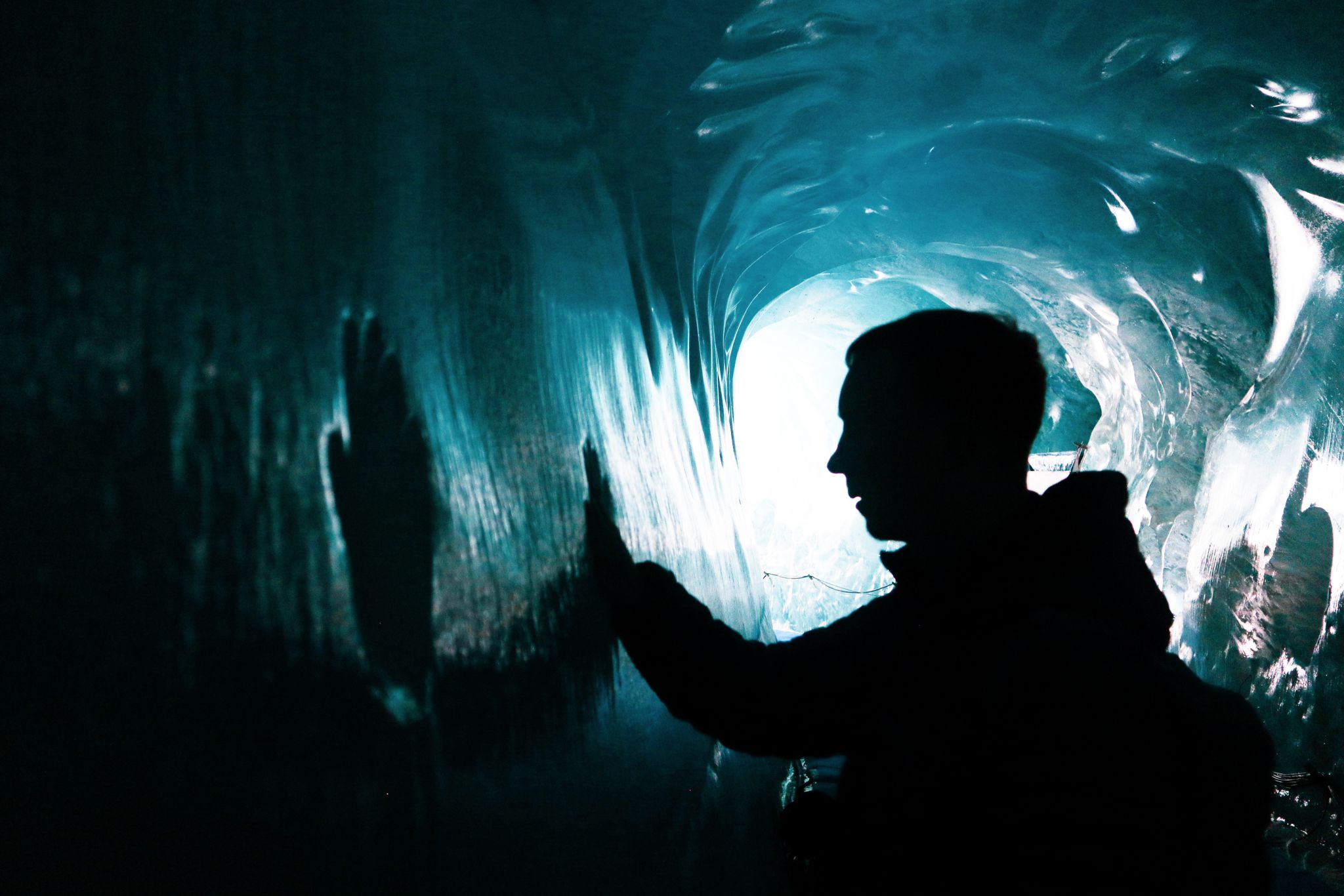 Winning entry shows shadowy glacier tunnel with a person holding their hands to the ice