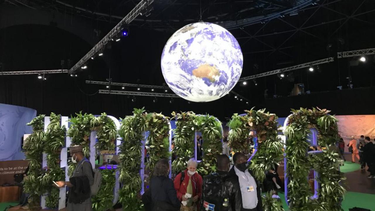 Sign made of plant's saying #COP26 with a suspended globe above in the COP26 entrance hallway.