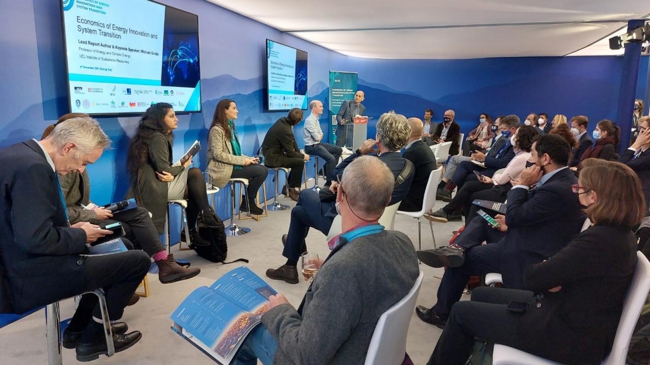 Launch of the Report at COP26 - numerous people in a room arranged in a panel lay out. TV screens on the wall with the report title.