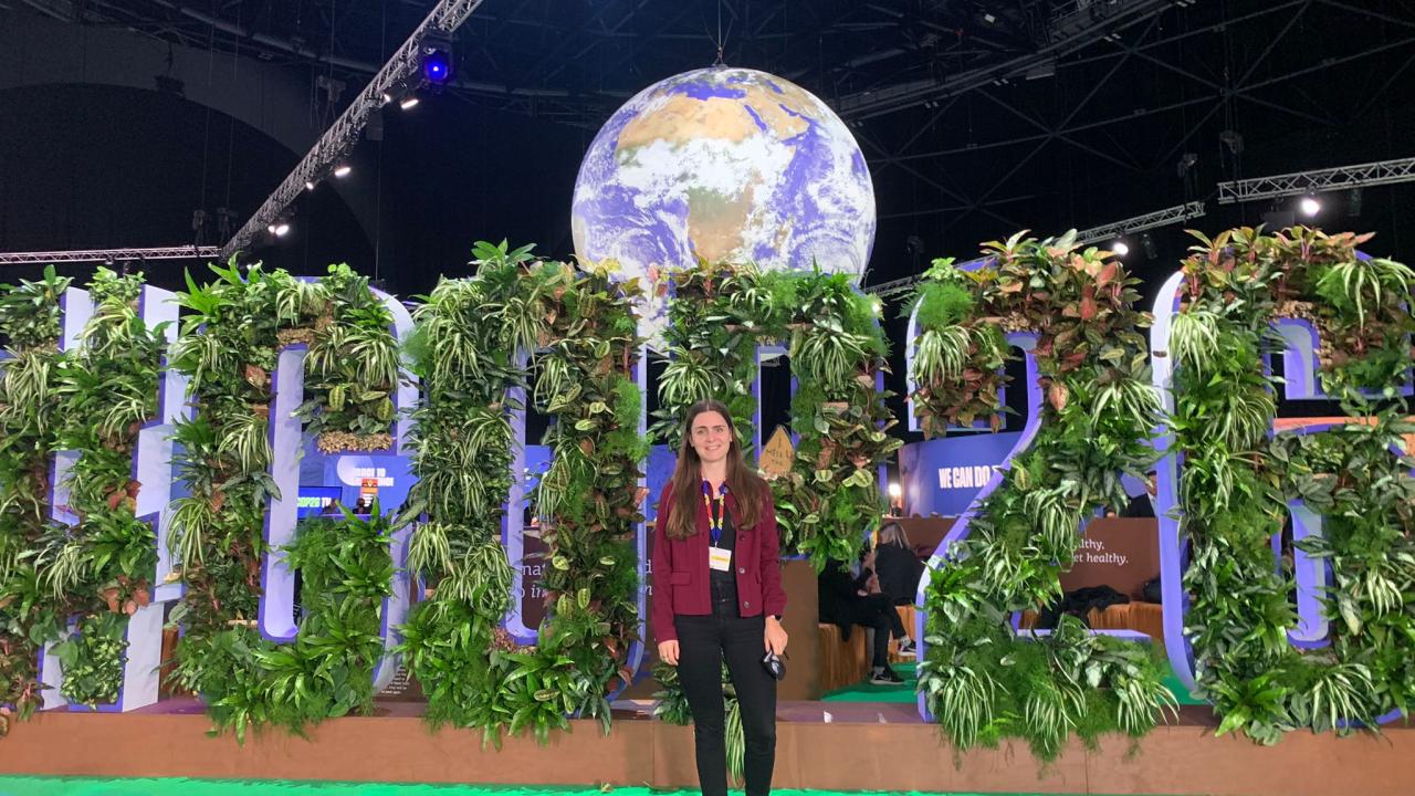 Friederike Hartz stands in front of the #COP26 sign made out of plants.