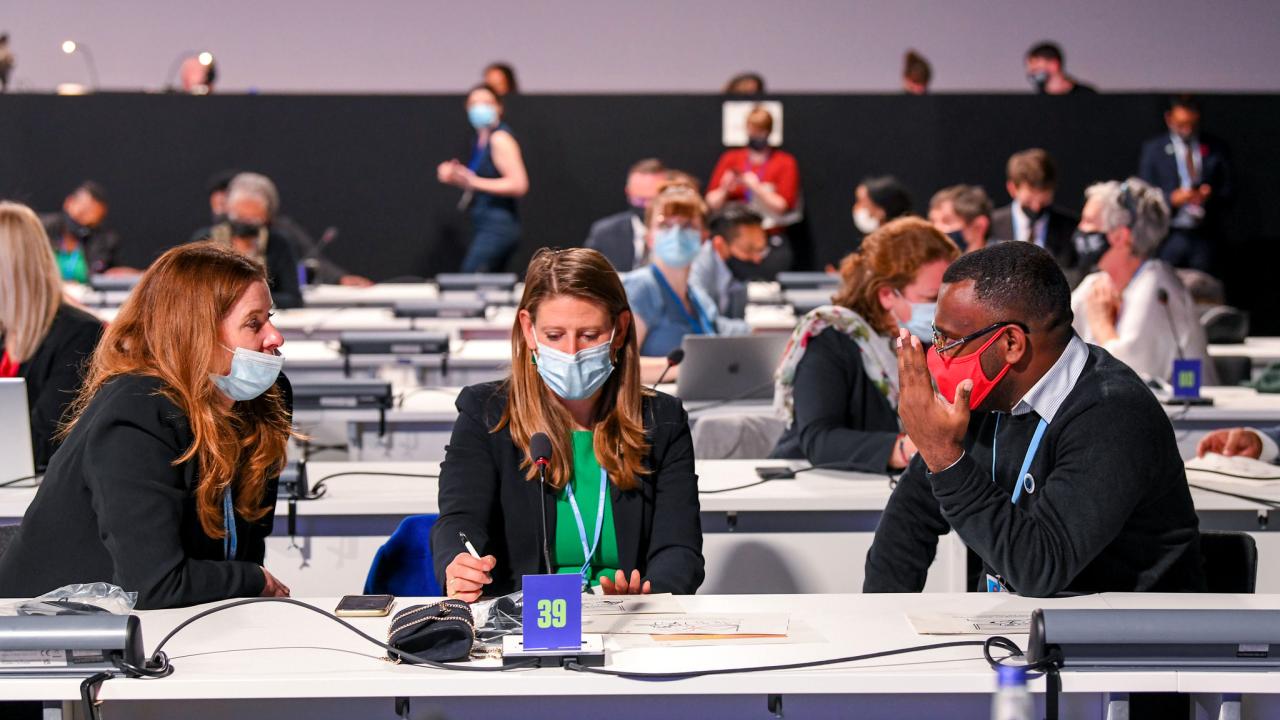 Three delegates have a conversation in the COP26 plenary room