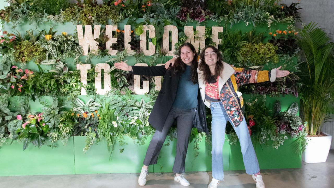 Rosa Prosser and friend in the Green Zone at COP26. Two women stand in front of a sign made of green plants reading 'Welcome to COP26'