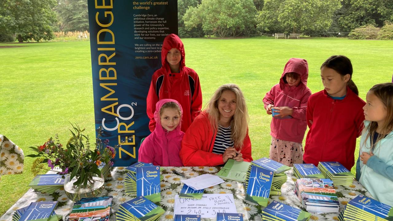 Prof Emily Shuckburgh sits at a table of books surrounded by children