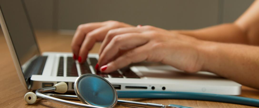 Person typing and stethoscope next to it. Photo by National Cancer Institute on Unsplash