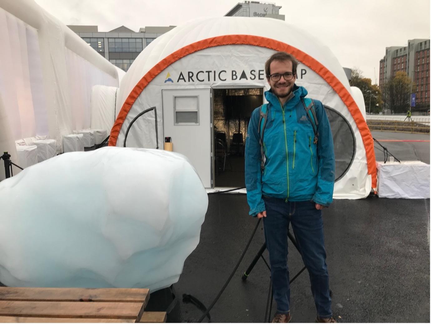 Dr Erik Mackie stands next to a large chunk of ice outside COP26's arctic basecamp.