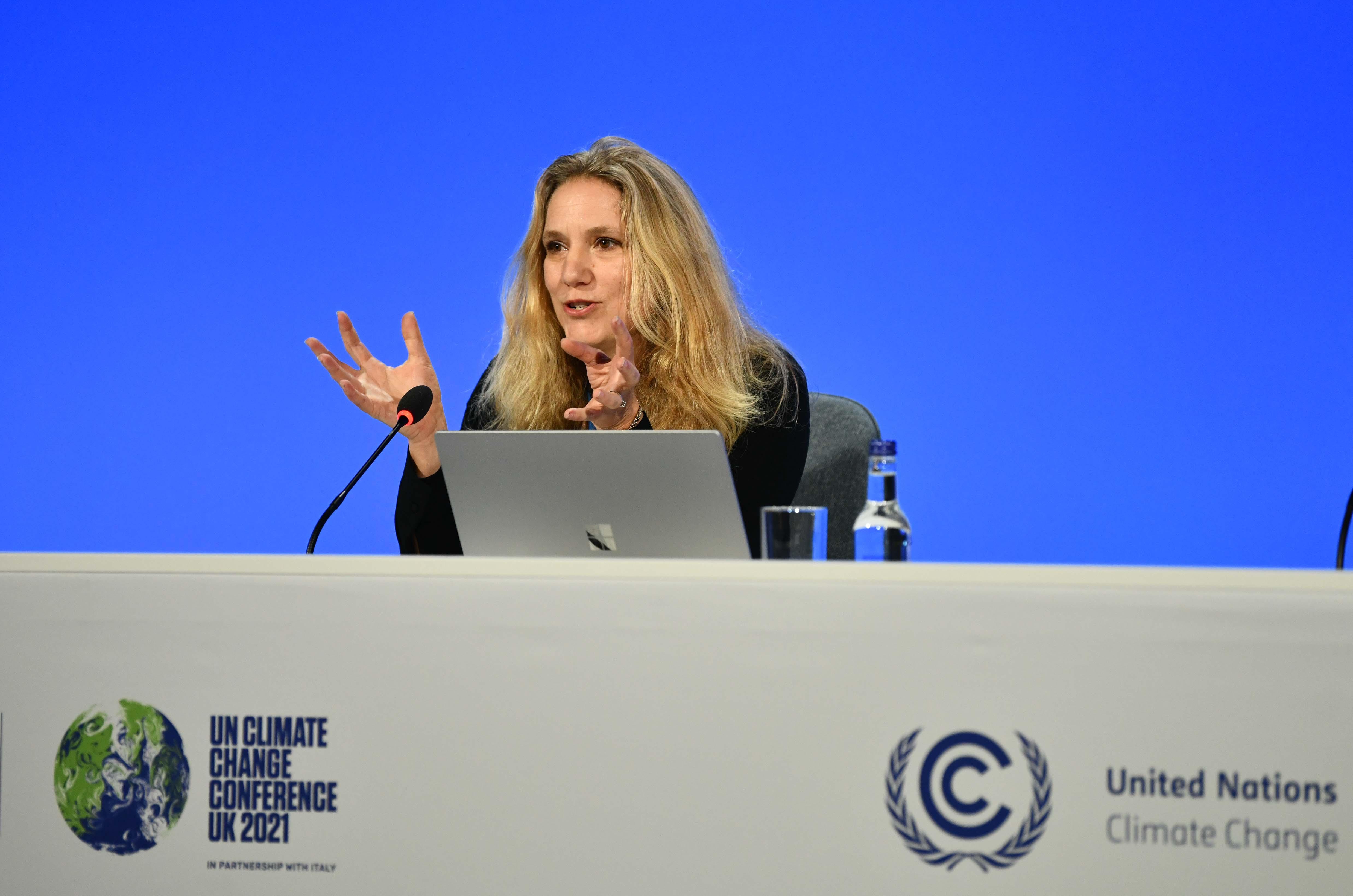 Professor Emily Shuckburgh sits behind her laptop and gestures while speaking on a panel at COP26. The background is white and the table she is sat at is adorned with UN COP26 logos. 