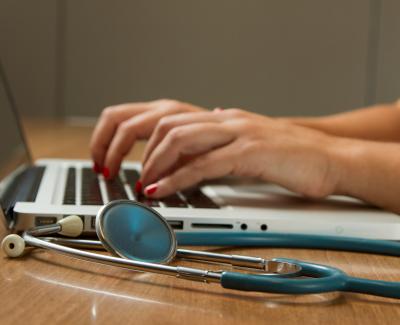 Person typing and stethoscope next to it. Photo by National Cancer Institute on Unsplash